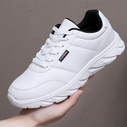 White sneaker with black accents held by a hand against a gray background