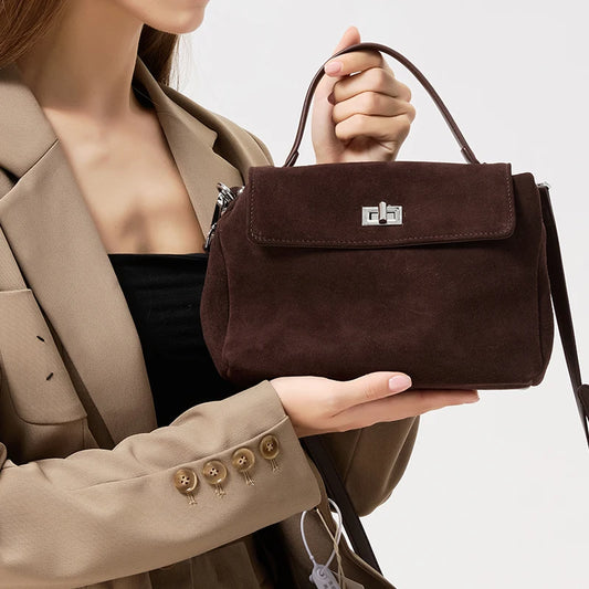 Brown handbag held by a person wearing a beige coat on a light background